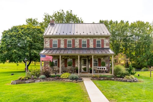 Front view of a stone farmhouse with red shutters, a covered porch and stone walkway