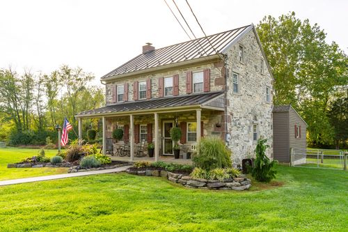 Stone farmhouse exterior with red shutters, a covered porch and an attached storage shed
