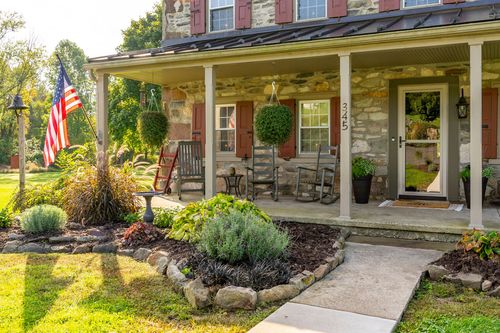 Front porch of a stone farmhouse with an American flag, potted topiaries and rocking chairs