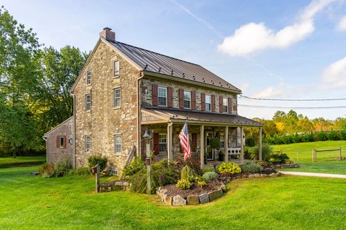 Side view of a stone farmhouse with a covered porch, American flag and landscaped stone beds
