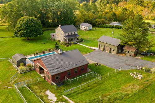 Aerial view of a stone farmhouse with a pool, red barn and detached garage surrounded by pasture