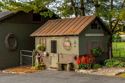 Rustic garden shed with a copper roof, wreath decor and colorful potted flowers