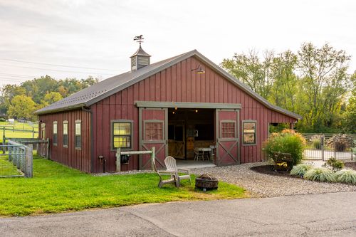 Red bank barn exterior with a cupola, sliding doors and a stone fire pit seating area