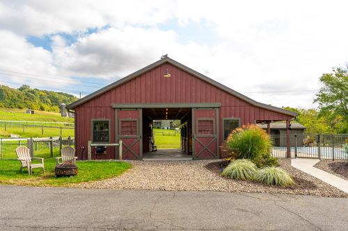 Red bank barn with open sliding doors revealing an interior seating area and pool beyond