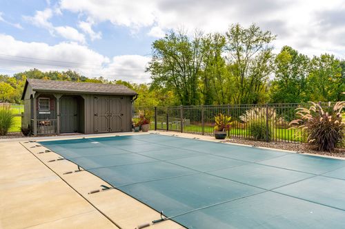 Covered pool with a storage shed and wrought iron fencing surrounded by landscaping