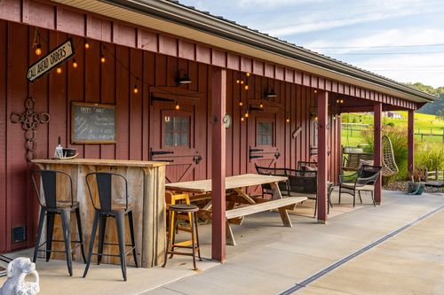 Covered outdoor bar with string lights, a chalkboard menu and seating along a barn's porch