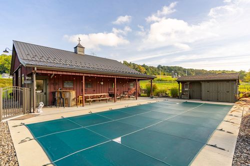 Covered pool beside a red barn with an attached storage shed and porch seating