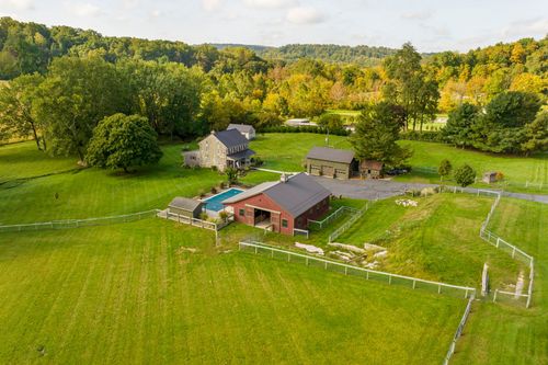 Aerial view of a stone farmhouse, pool and red barn nestled among trees and green farmland