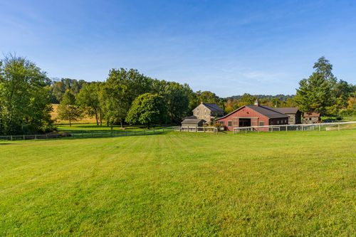 Distant view of a red barn and stone farmhouse across an open grassy field