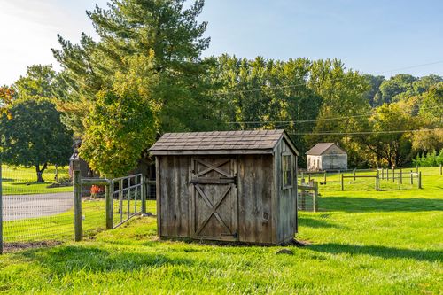 Weathered wood storage shed with a peaked roof set beside a fenced pasture