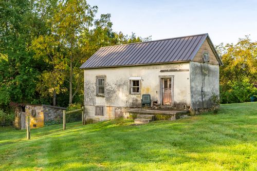 Weathered stucco outbuilding with a metal roof and rustic wood door
