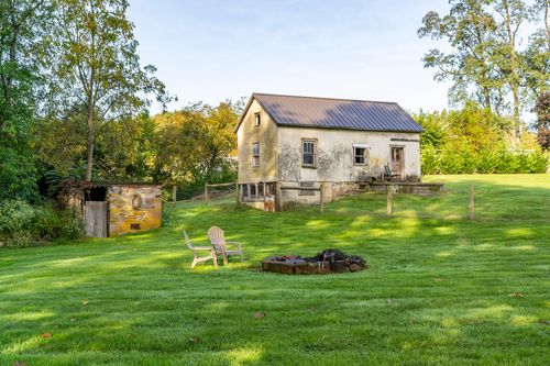 Weathered stucco outbuilding beside a fire pit with Adirondack chairs on the lawn