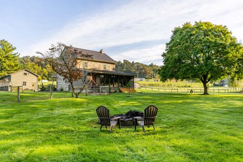 Stone farmhouse viewed across a lawn with a fire pit and Adirondack chairs