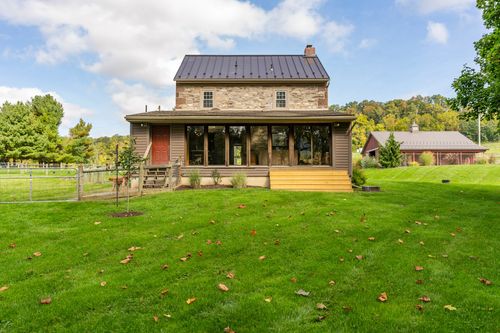 Rear exterior of a stone farmhouse with a covered deck and metal roof