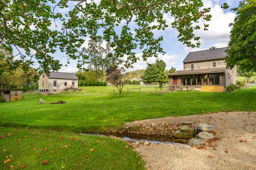Stone farmhouse and outbuilding beside a small stone-lined creek crossing the lawn