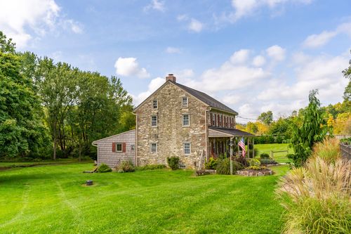 Side exterior of a stone farmhouse with an American flag and landscaped stone borders
