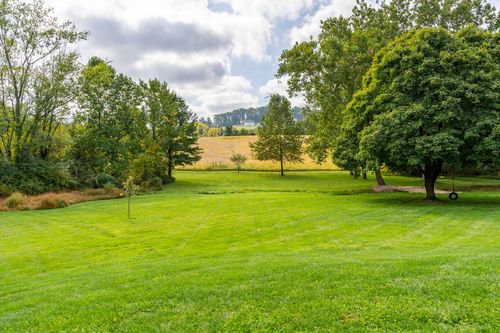 Open lawn framed by mature trees with distant farmland and a tire swing