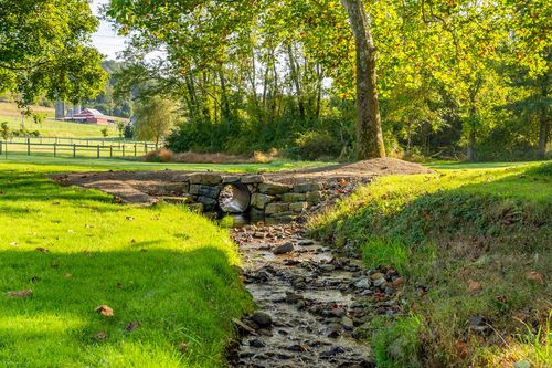 Stone footbridge arching over a small rocky creek bed lined with trees