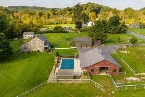 Aerial view of a stone farmhouse, pool and red barn with a garage and workshop building nearby