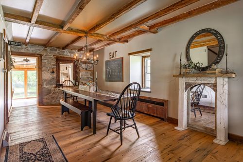 Farmhouse dining room with exposed wood beams, a stone fireplace and a long farm table with Windsor chairs