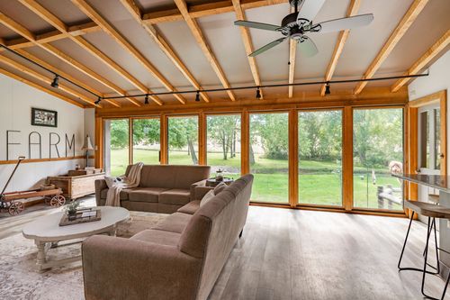 Vaulted sunroom with exposed wood beams, a ceiling fan, wagon wheel decor and a wall of windows
