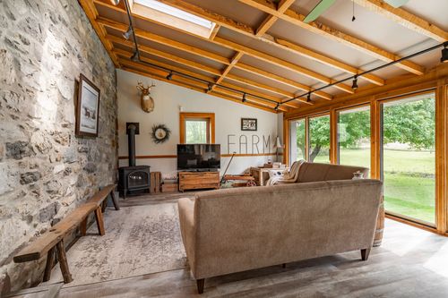 Living room with a stone accent wall, wood stove and mounted deer antlers beneath vaulted beams