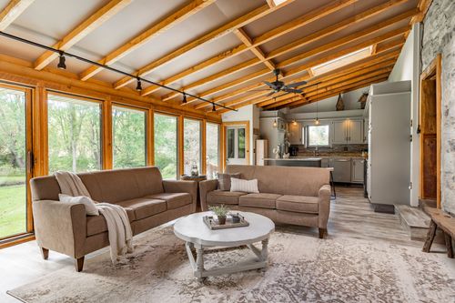 Great room with vaulted wood beam ceiling, stone wall and sectional sofas open to the kitchen