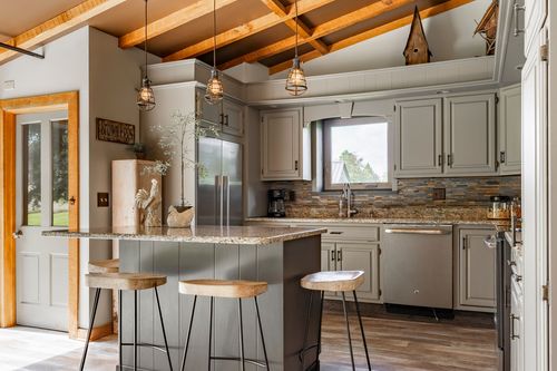 Kitchen with gray cabinetry, granite island, stainless appliances and pendant lighting under wood beams