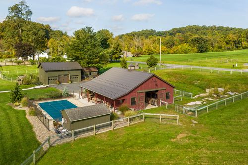 Aerial view of a stone farmhouse, pool and red bank barn framed by a horseshoe gravel drive