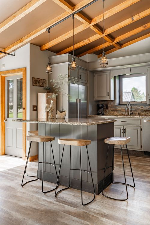 Kitchen island with a granite countertop, wood bar stools and pendant lights beneath an open beam ceiling