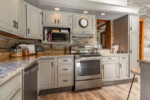 Kitchen with gray cabinets, stone accent wall, wall clock and stainless range