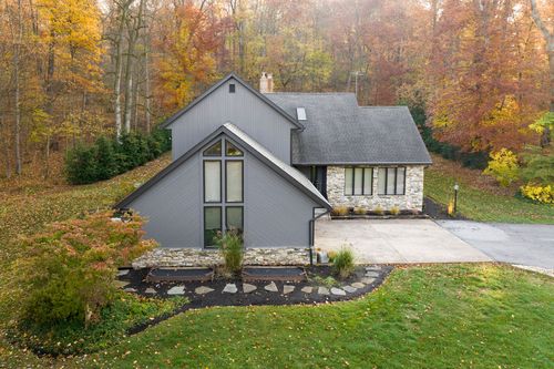 Aerial view of a gray board-and-batten home with stone accents amid fall foliage