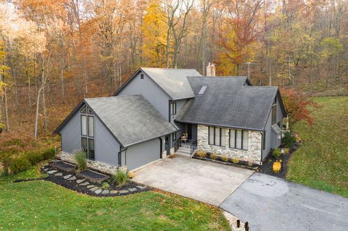 Aerial view of a gray farmhouse-style home with A-frame gables and autumn trees