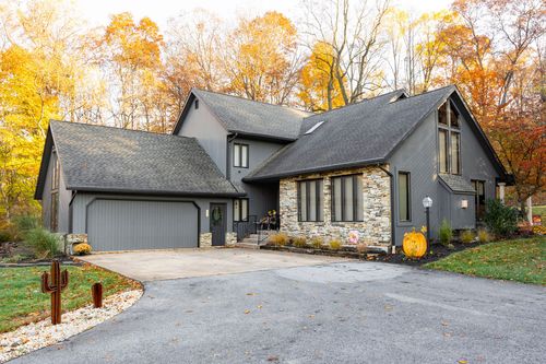 Gray home with stone chimney accent, gabled roofline and covered entry in fall trees