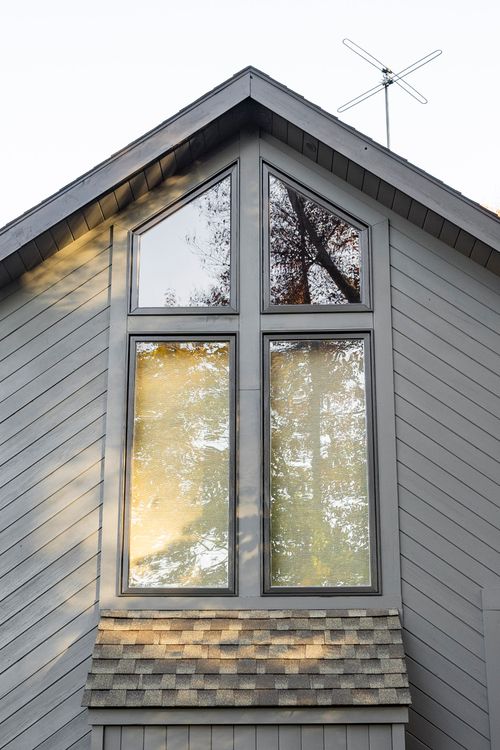 Close-up of a peaked gable window with dark trim reflecting autumn trees