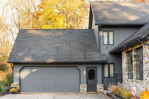 Two-story home exterior with dark garage door, stone accents and arched glass entry door