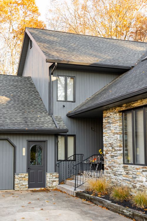 Gray home exterior with arched glass door, stone base and wrought-iron handrail steps
