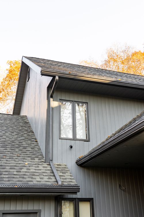 Close-up exterior view of gray board siding, gabled roofline and gutters