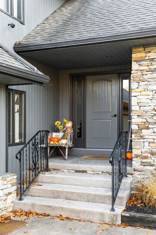 Covered front porch with gray door, stone columns and pumpkin fall decor