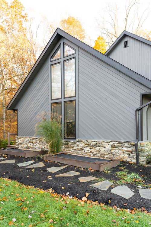 Close-up exterior of a steep gray gable with tall peaked window and stone base