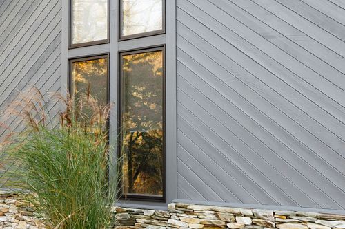 Close-up of a paned window reflecting autumn trees on diagonal gray siding
