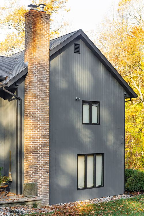 Close-up of a tall brick chimney beside gray board-and-batten siding