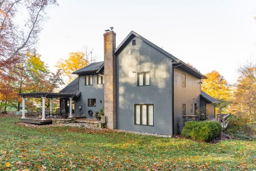 Home exterior with brick chimney, pergola patio and back deck amid autumn woods