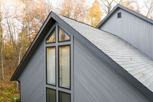Close-up aerial of a gray gabled roofline with large peaked window amid autumn trees