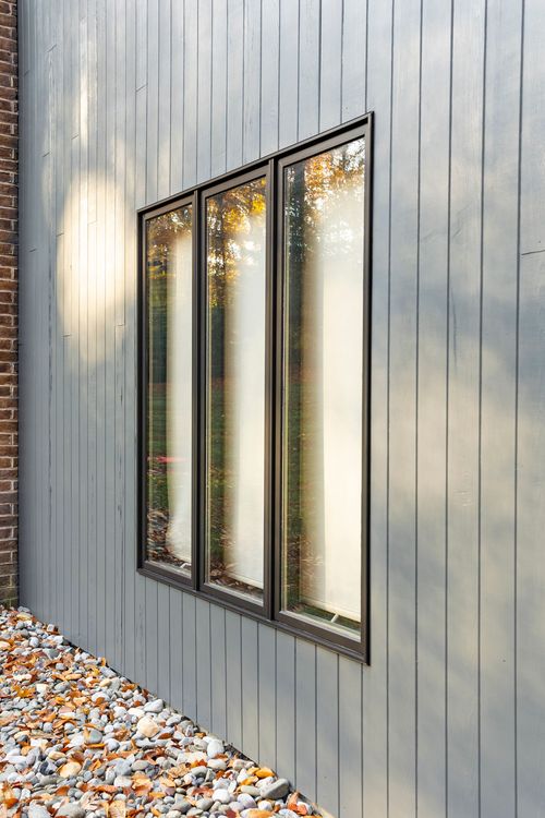 Close-up of tall paned windows on gray board-and-batten siding beside a brick wall