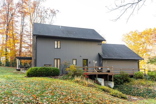 Home exterior with wraparound deck, board-and-batten siding and wooded hillside backdrop