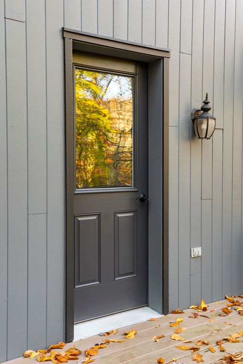 Close-up of a gray paneled back door with glass pane and lantern sconce