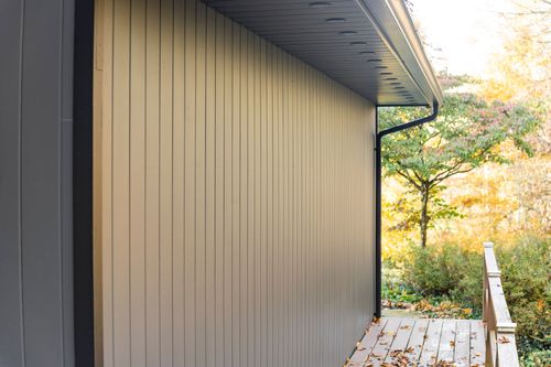 Close-up of tan board-and-batten siding corner with gutter and deck railing