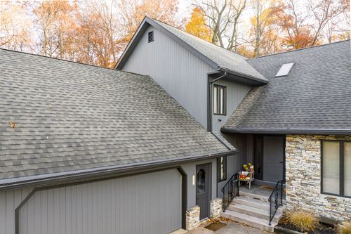 Aerial view of a gray home's rooflines, stone chimney and covered entry in fall