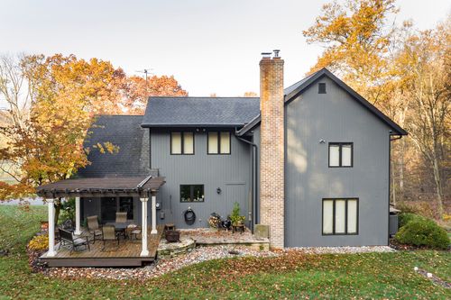 Home exterior with covered pergola patio, brick chimney and fall-colored trees